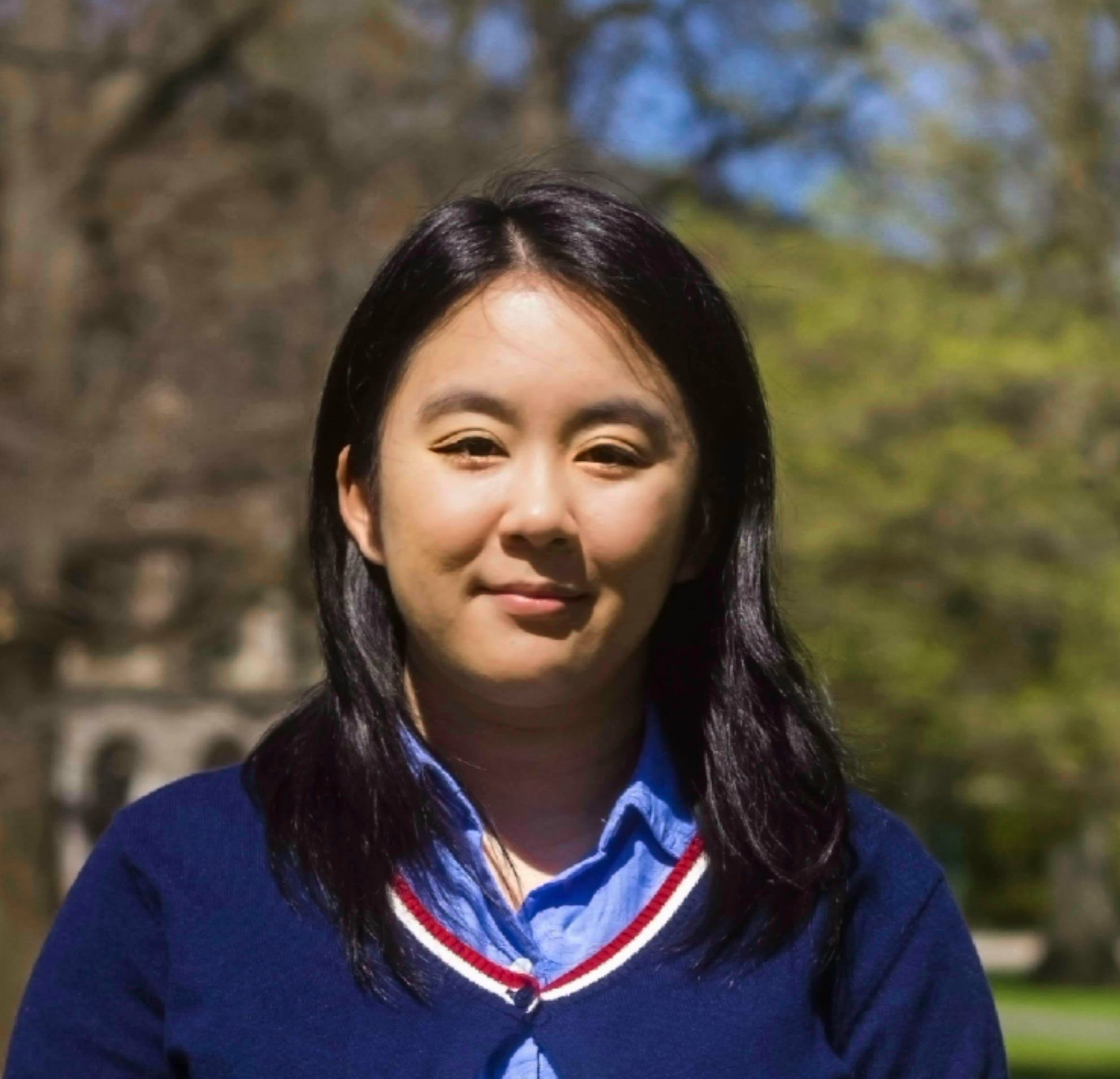 Headshot of Kelly Luo with green trees and school building in the background