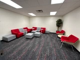 Photo of seating area in lounge. Red and grey color blocked couch, red armchairs and tree in corner.