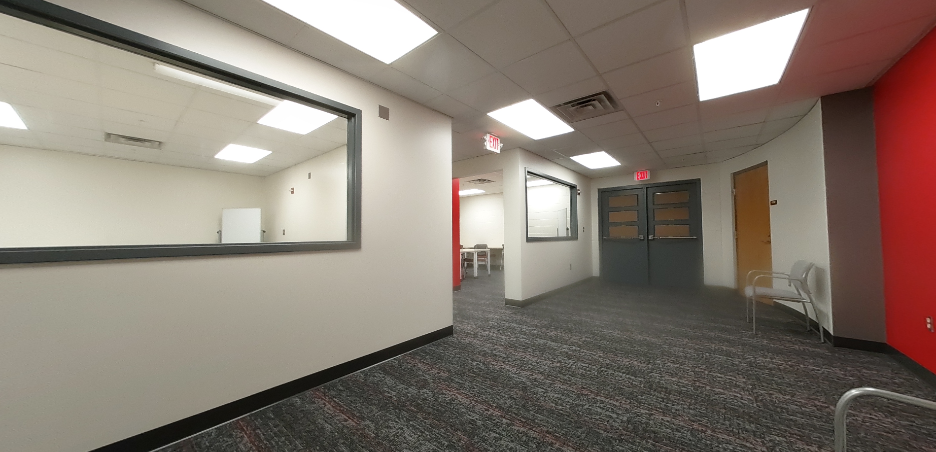 "After" photo of east entrance. Red accent wall, bright lighting, open space in hallway. "Windows" into well lit, inviting study rooms.