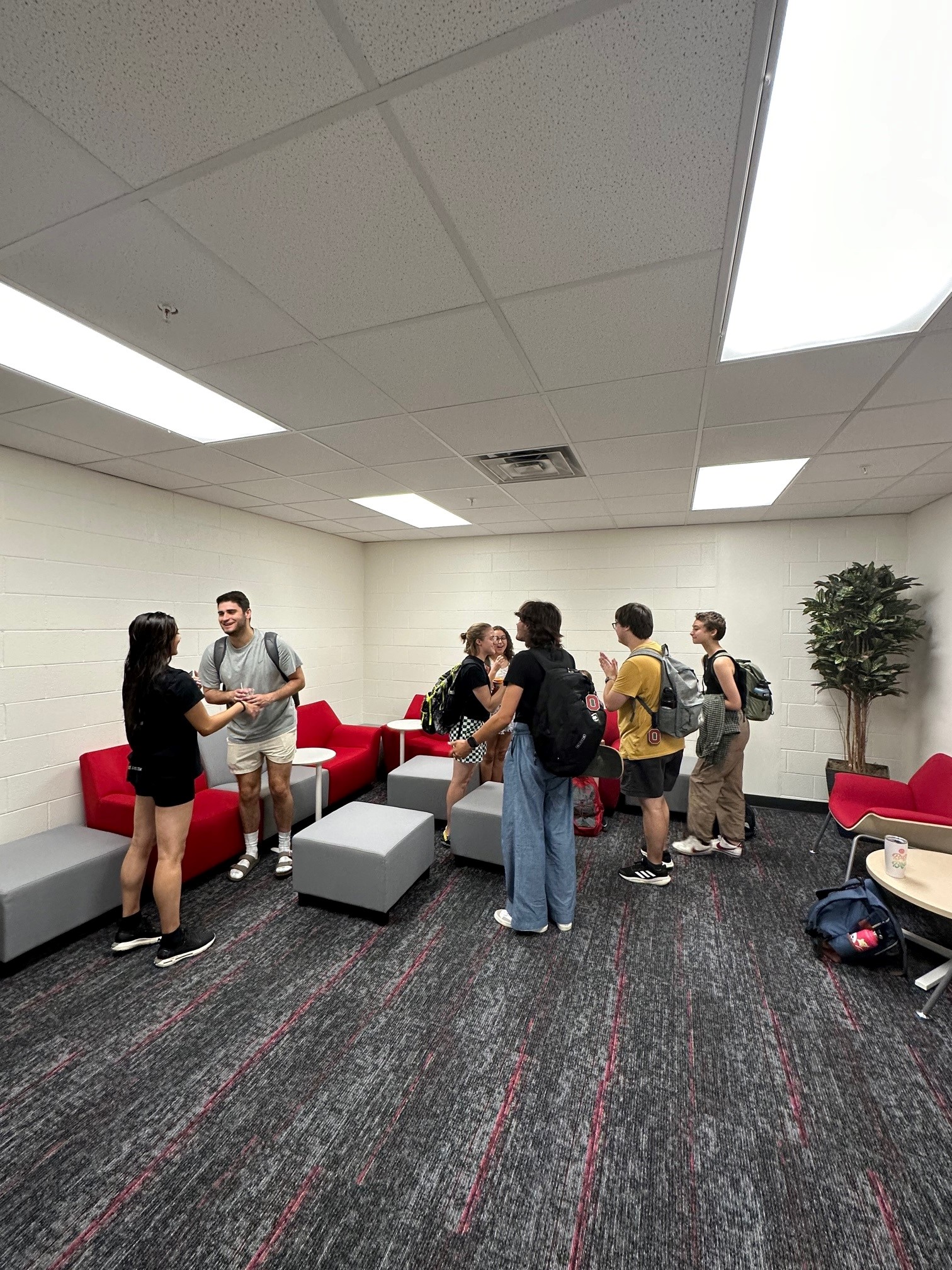 Photo of students talking and laughing in room with red and grey couch