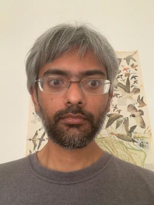 Sarang Gopalakrishnan in front of a beige wall and bird poster