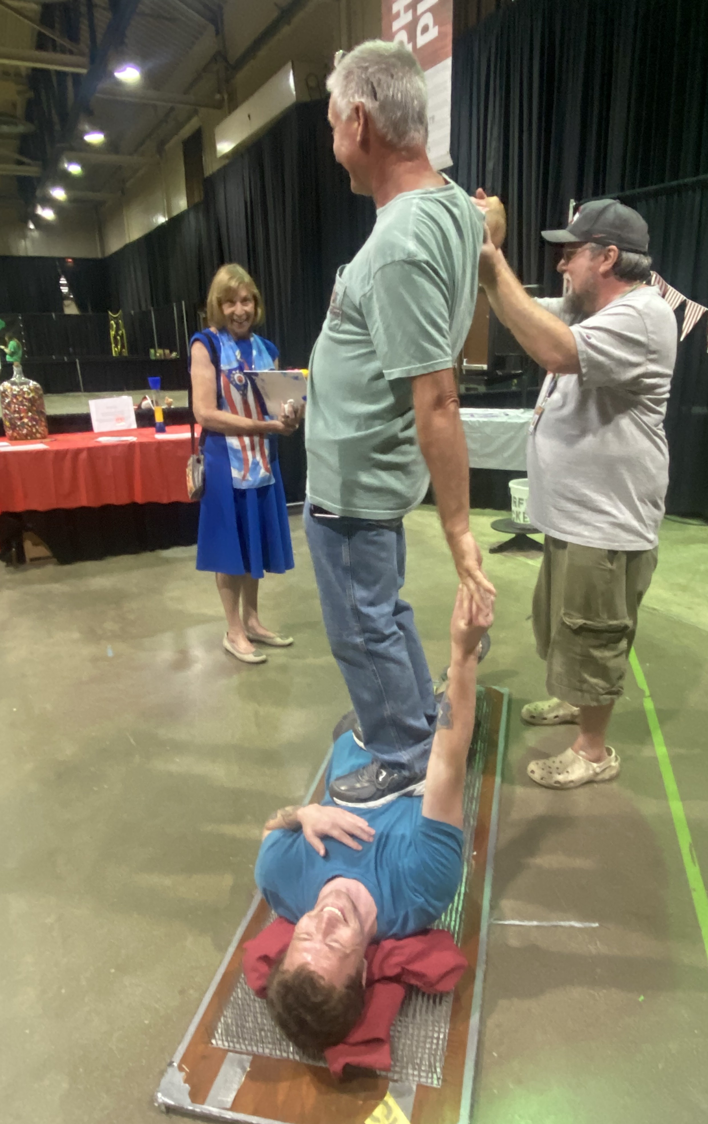 A person stands on Alex while he lays on the bed of nails