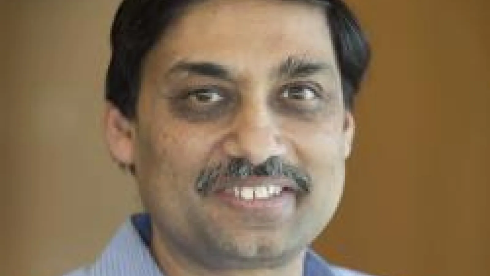 Samir Mathur smiling with brown background