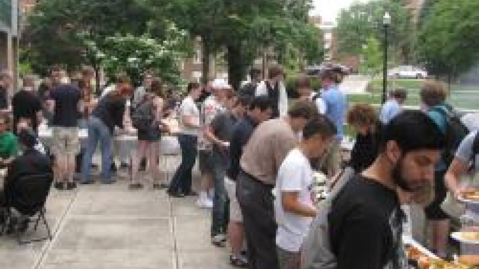 A picture from the physics picnic with students gathered around tables with food in a buffet style setting. 