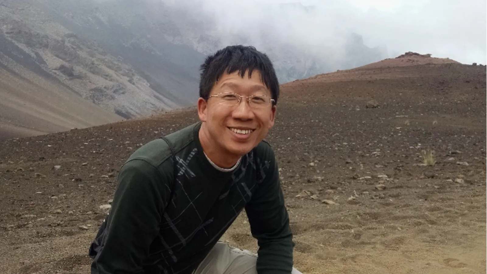 Chen Wang crouching with mountains in the background