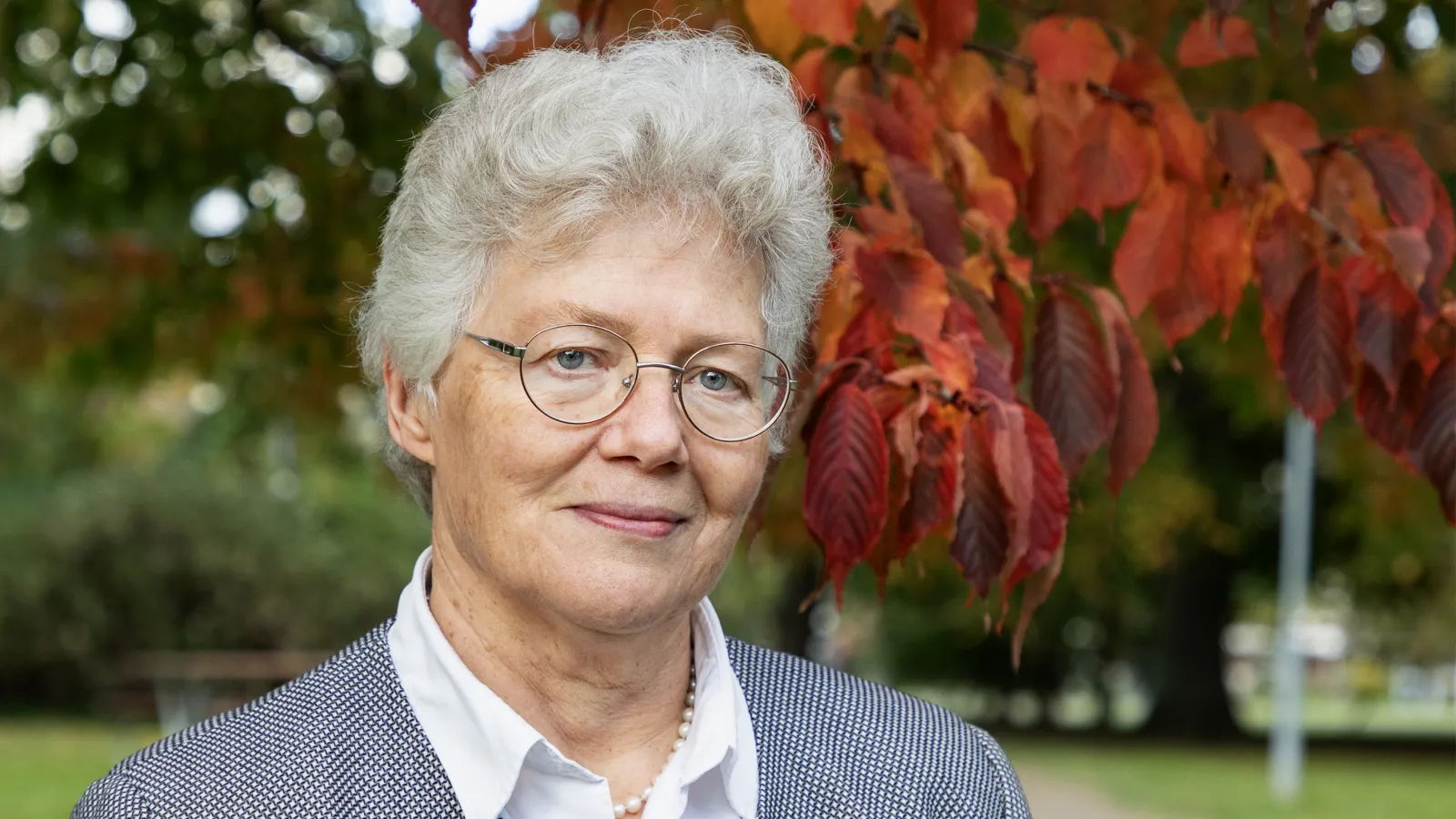 Anne L'Huiller pictured in front of tree with bright orange leaves behind her.