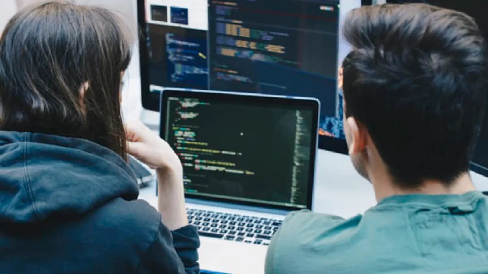 Photo looking over the shoulder of two people coding and looking at a computer