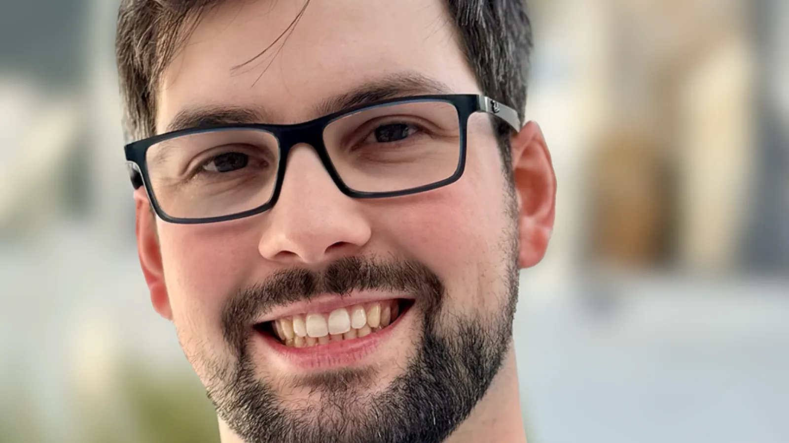 Alexander smiling in front of a blurred campus background