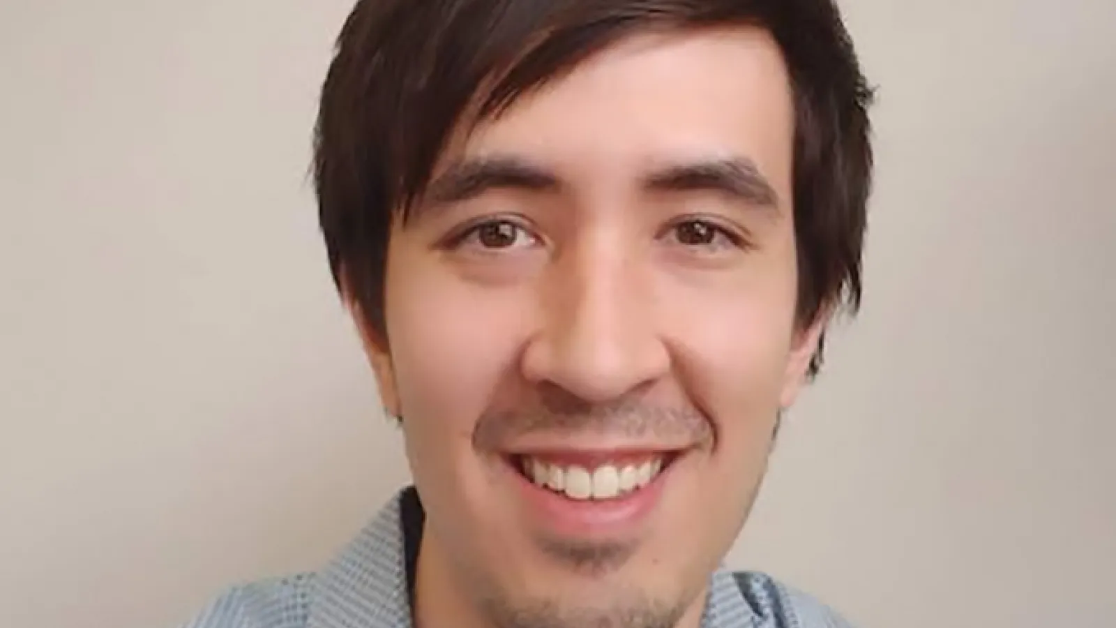 Matthew Low smiling in front of a plain beige wall