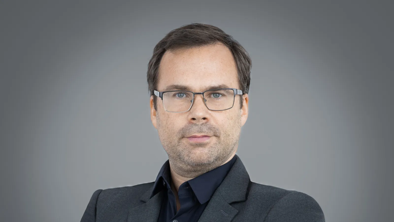 Nicolas standing with arms folded in front of a grey background