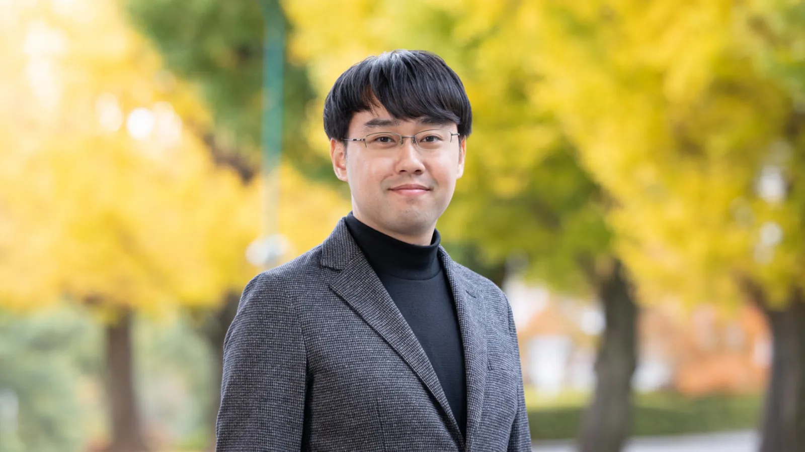 Yuki Fujimoto smiling and standing in front of a row of bright yellow trees