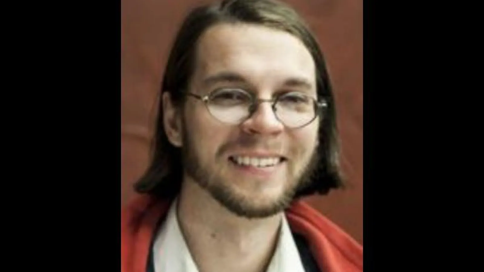 Chris Orban smiling with brown background and black frame border