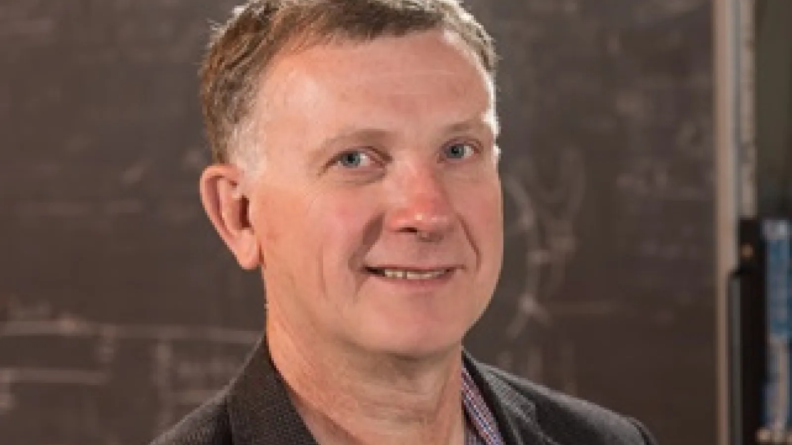 Headshot of Tomasz Skwarnicki smiling with a chalkboard background.