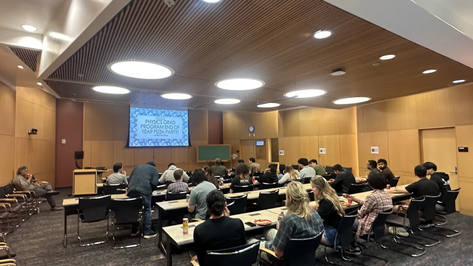 a conference room full of students sitting and eating pizza