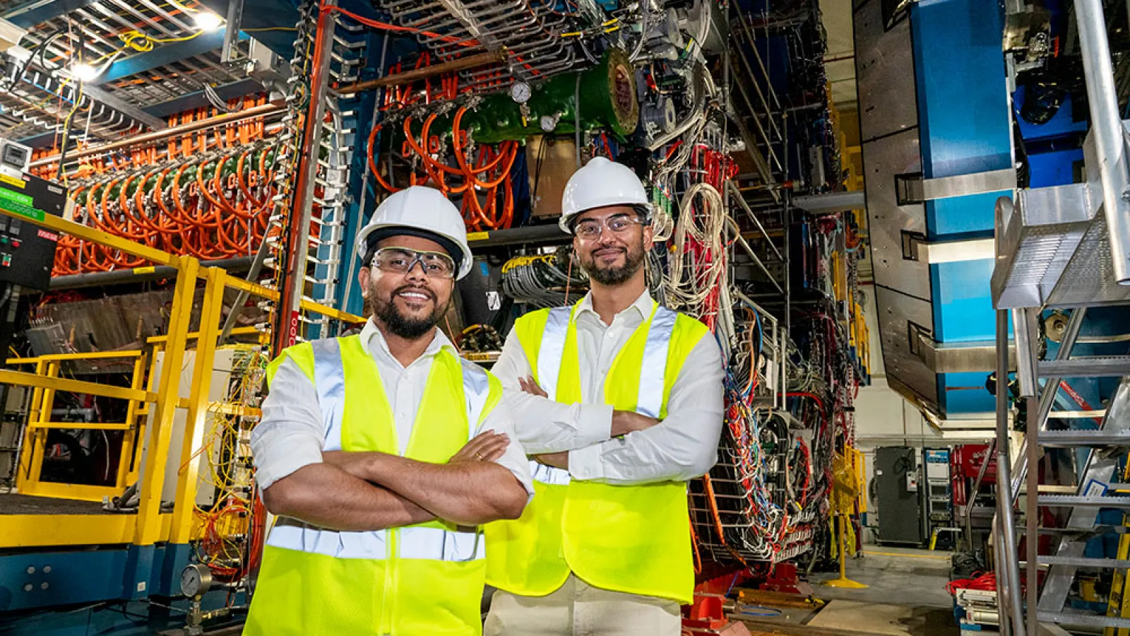 Kent State University postdoctoral research scientist Ashik Ikbal and Brookhaven Lab physicist Prithwish Tribedy stand in front of the STAR detector at the Relativistic Heavy Ion Collider (RHIC) at Brookhaven National Laboratory. The two were on a team that tracked the decay "daughters" of J/psi particles created in not-quite-colliding interactions of gold ions at RHIC. Their goal: Establish the foundation for using J/psi particles and their spin to map out the distribution of gluons within the ions. (David