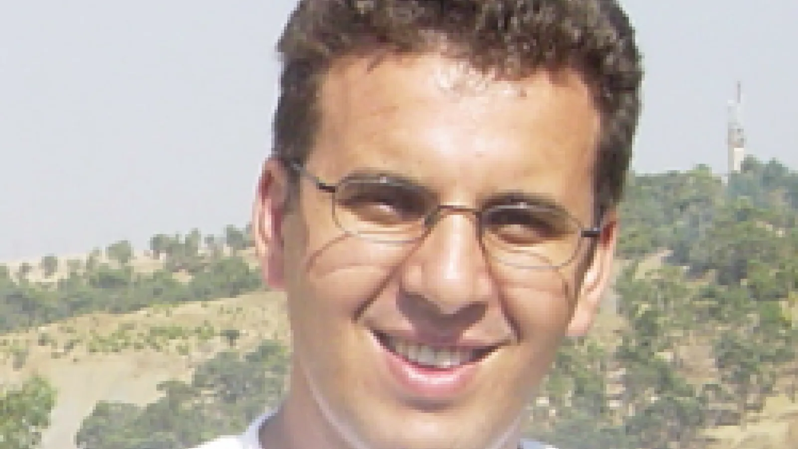 A close-up of Dr. Kramer Akli. The background contains trees and green hills.