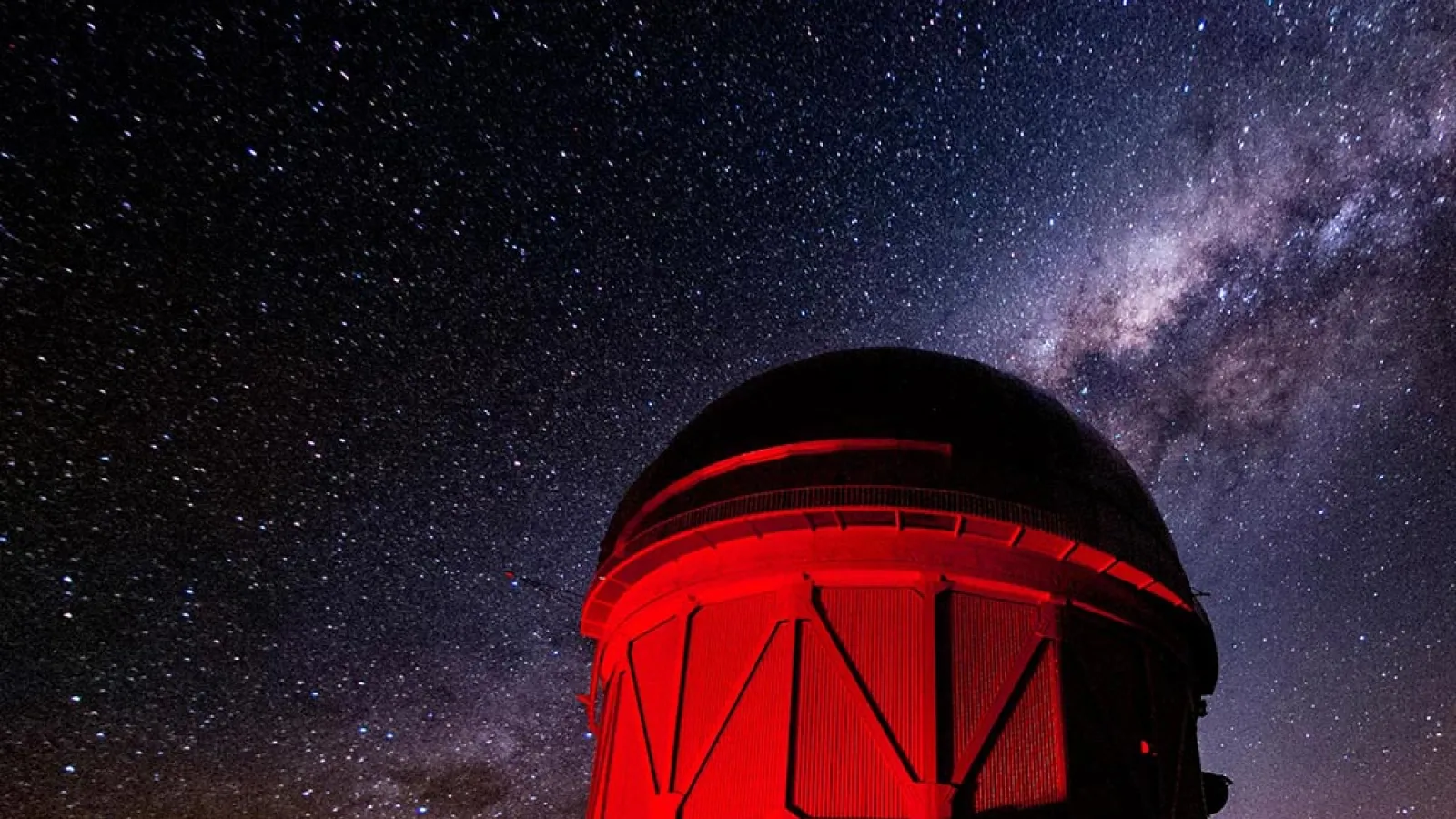 Large telescope lit up with red light and starry sky behind it