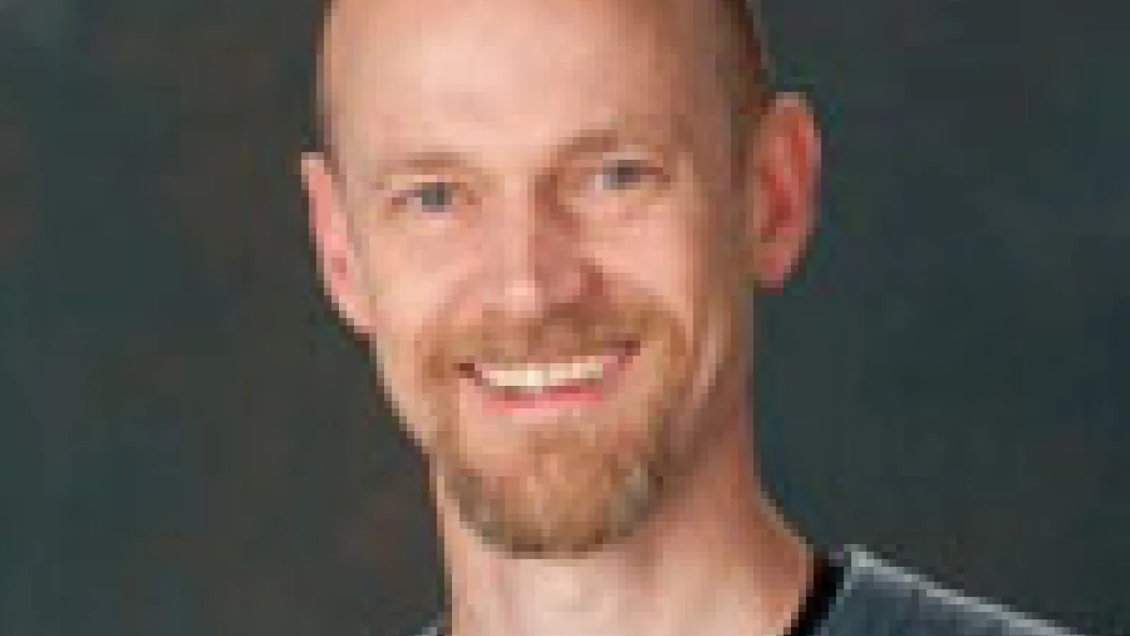John Beacom smiling with dark grey background