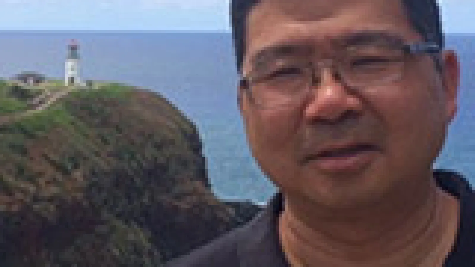 Roland Kawakami with lighthouse on a cliff far behind him