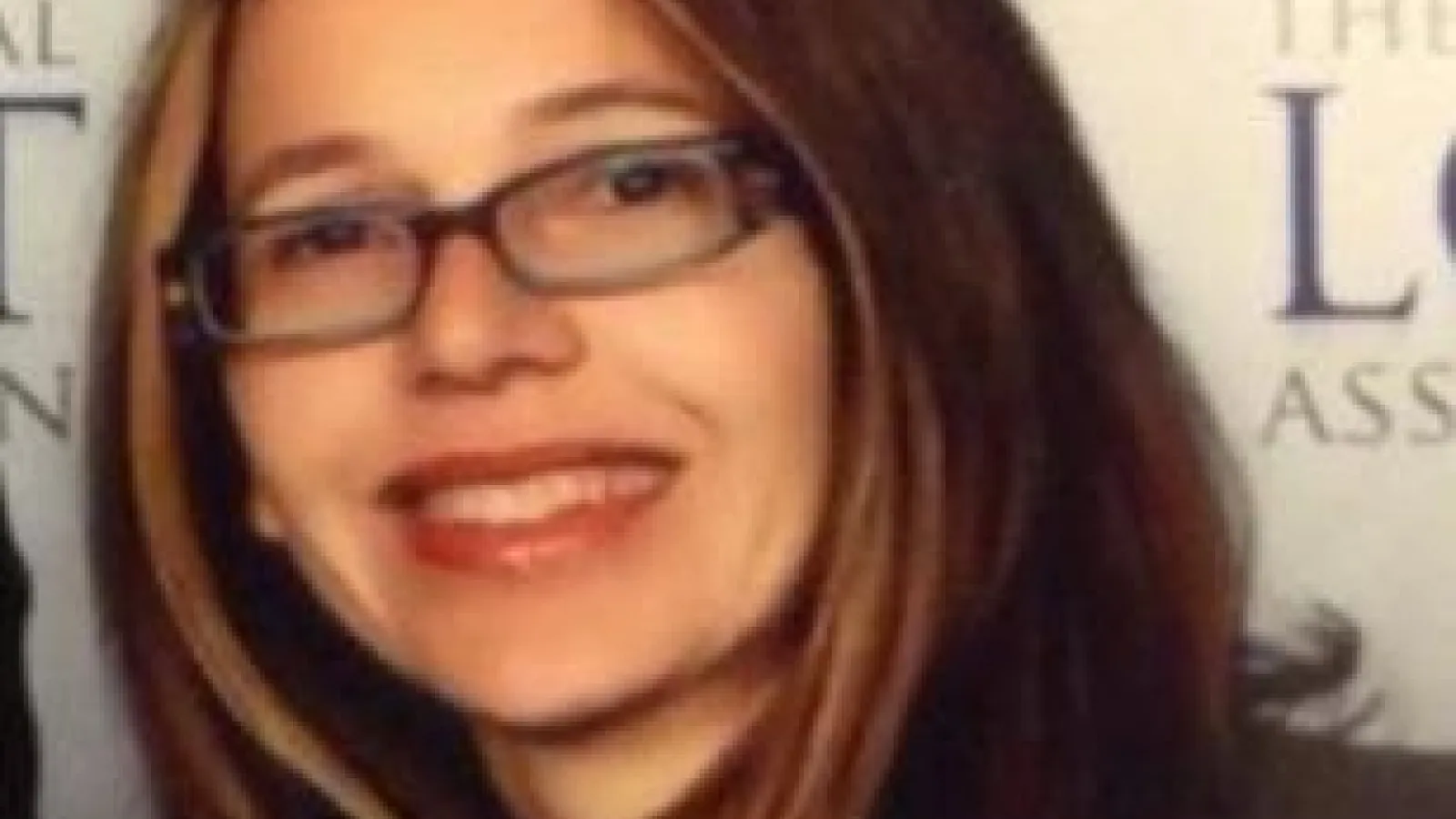 Paula Vivas smiling in front of a white wall with unintelligible words on it