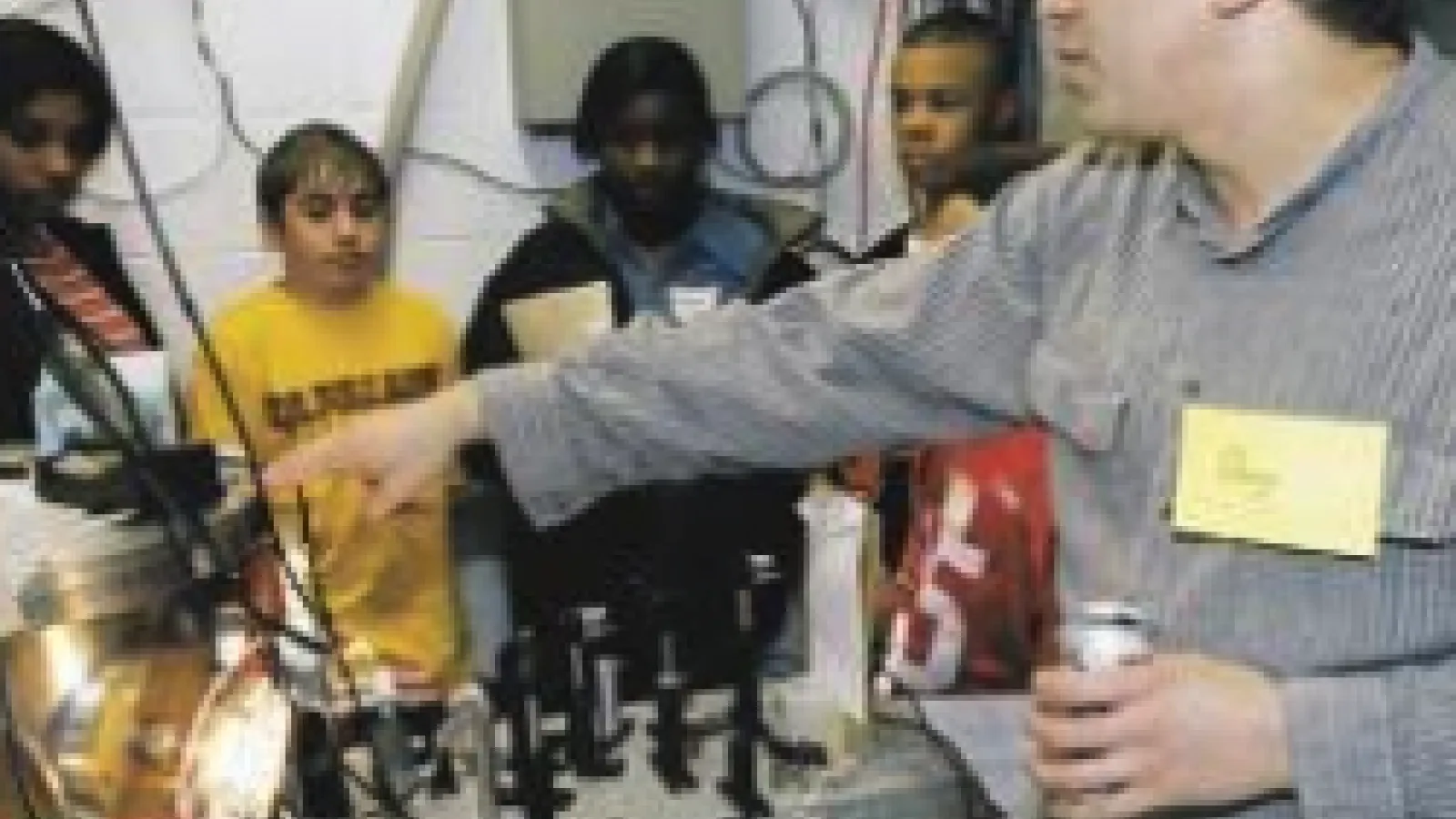 The picture shows Douglass Schumacher working with a group of students in a lab. He is explaining the equipment as the students listen attentively.