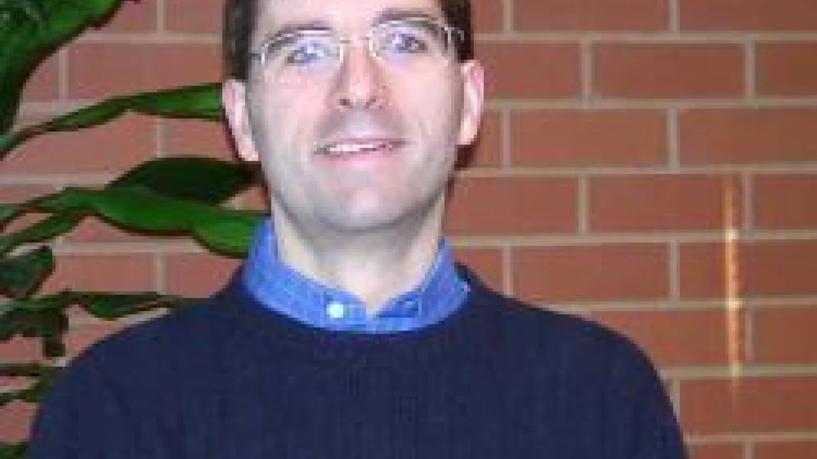 Bradley Ambrose with brick wall and potted plant behind him