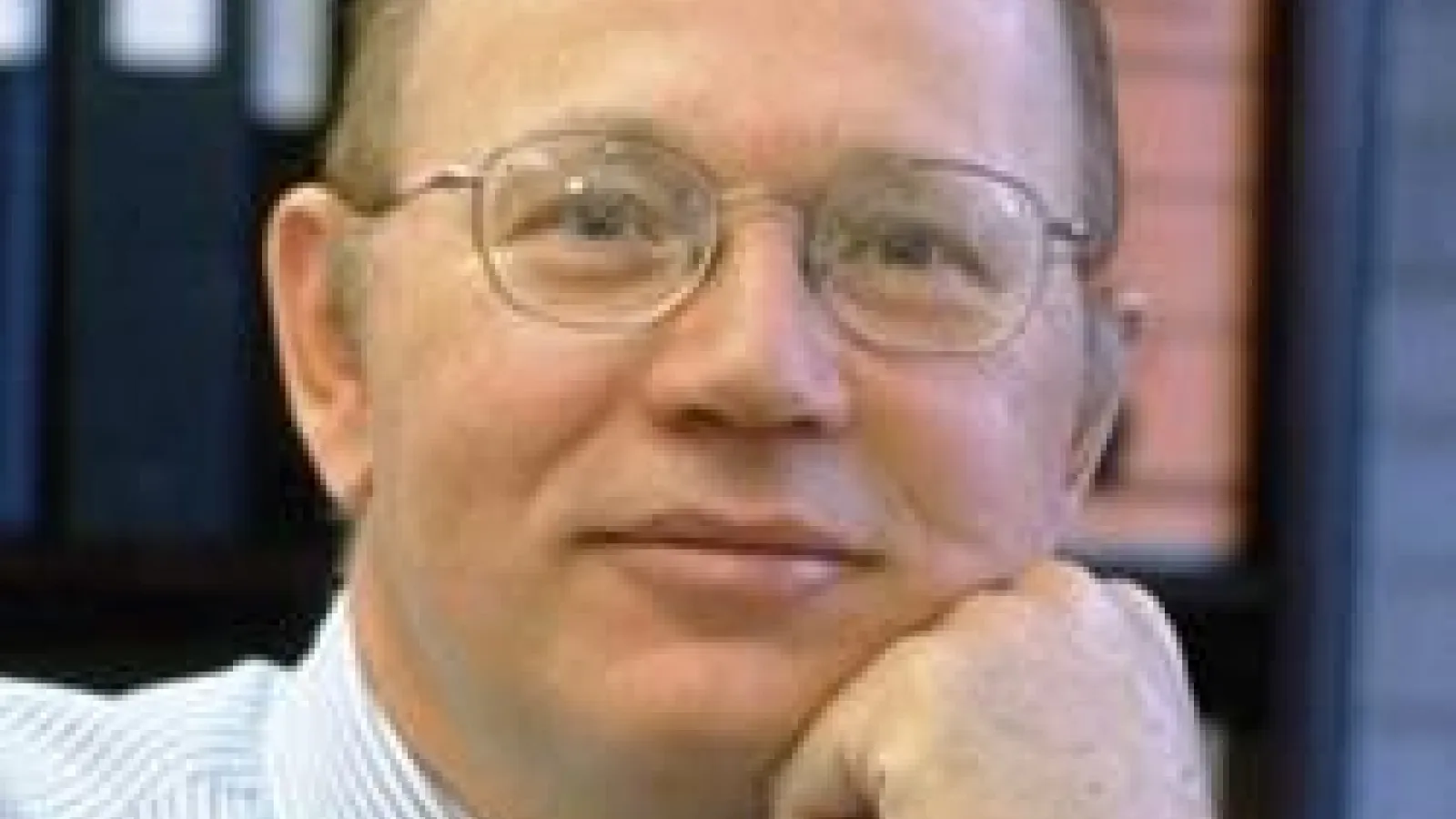 Brian Clark smiling with head on hand and bookshelf in the background