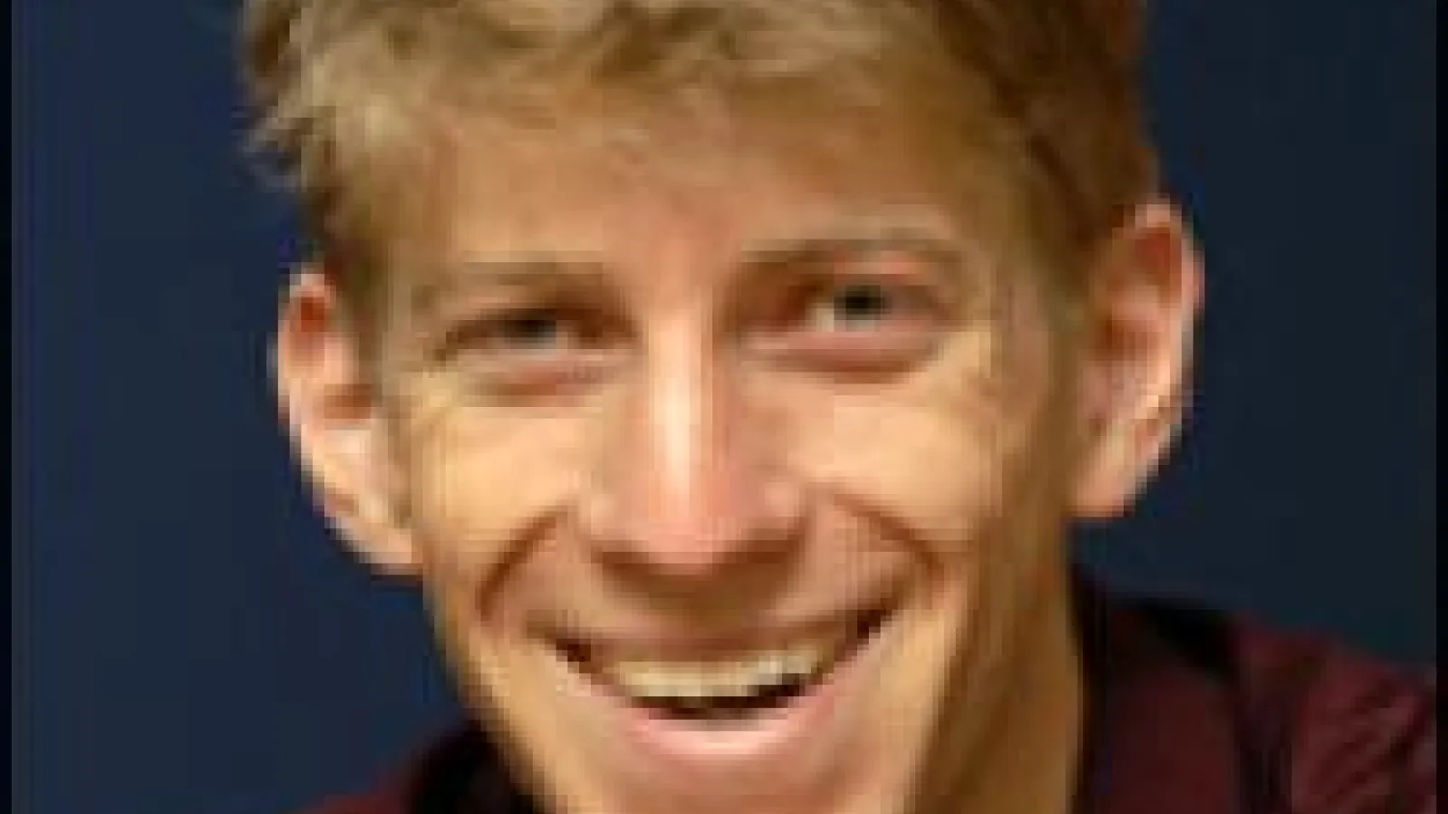 Blurry headshot of Adam Cohen smiling with navy background