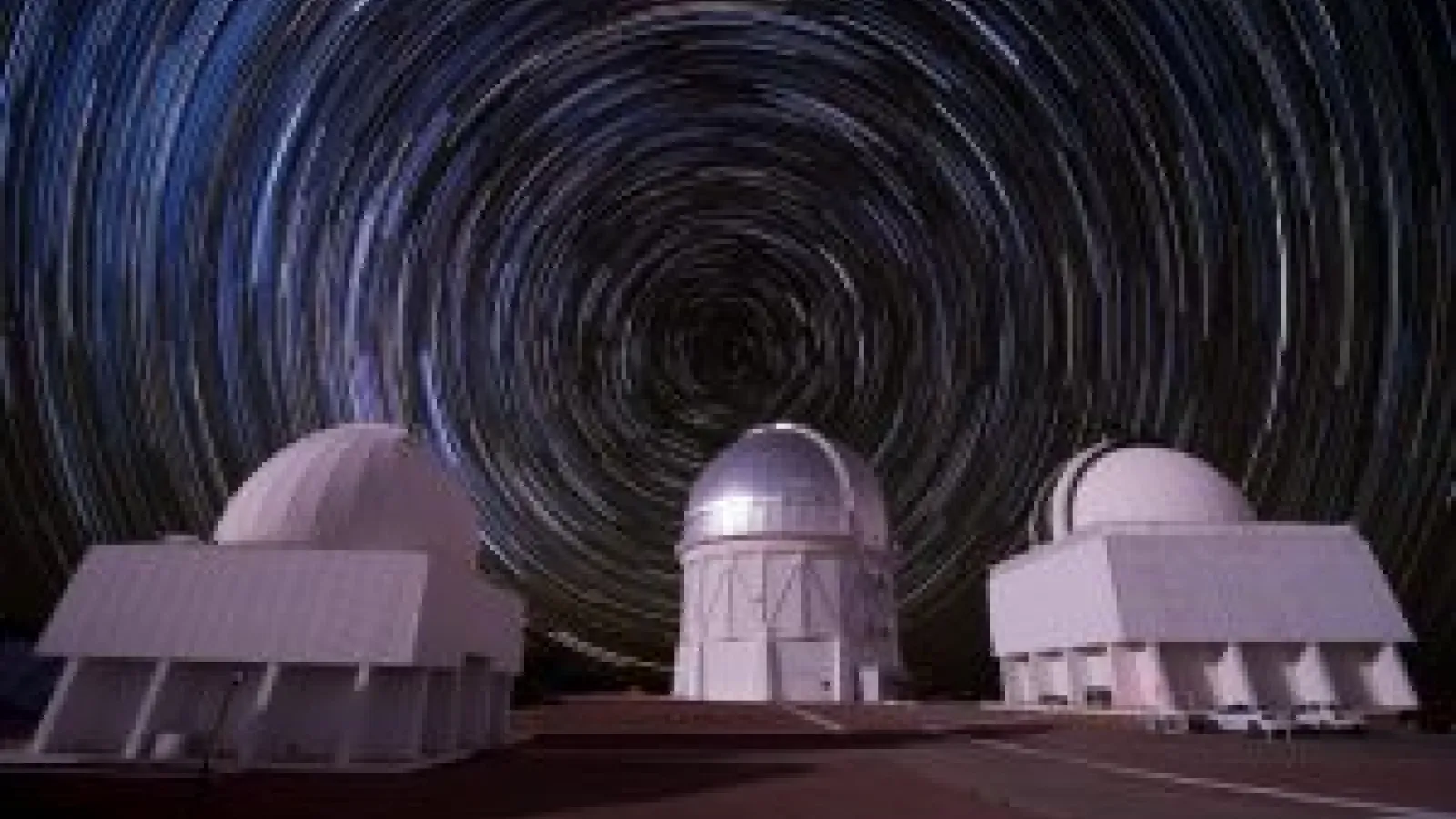 Three large white telescopes with sky swirling behind them