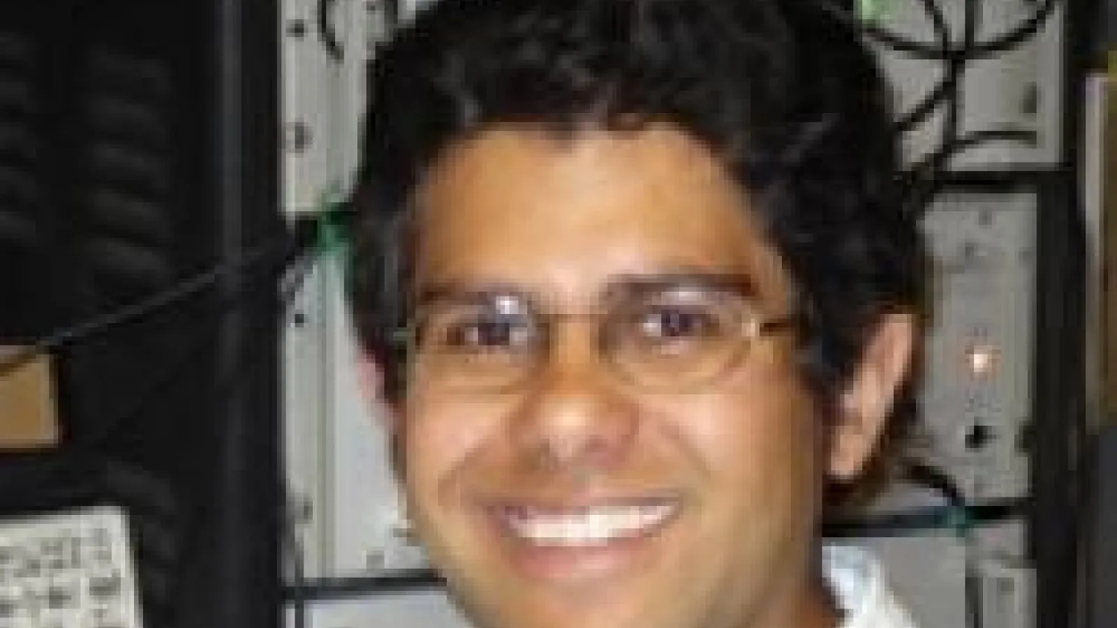 Jay Gupta smiling and standing in front of computer hard drive
