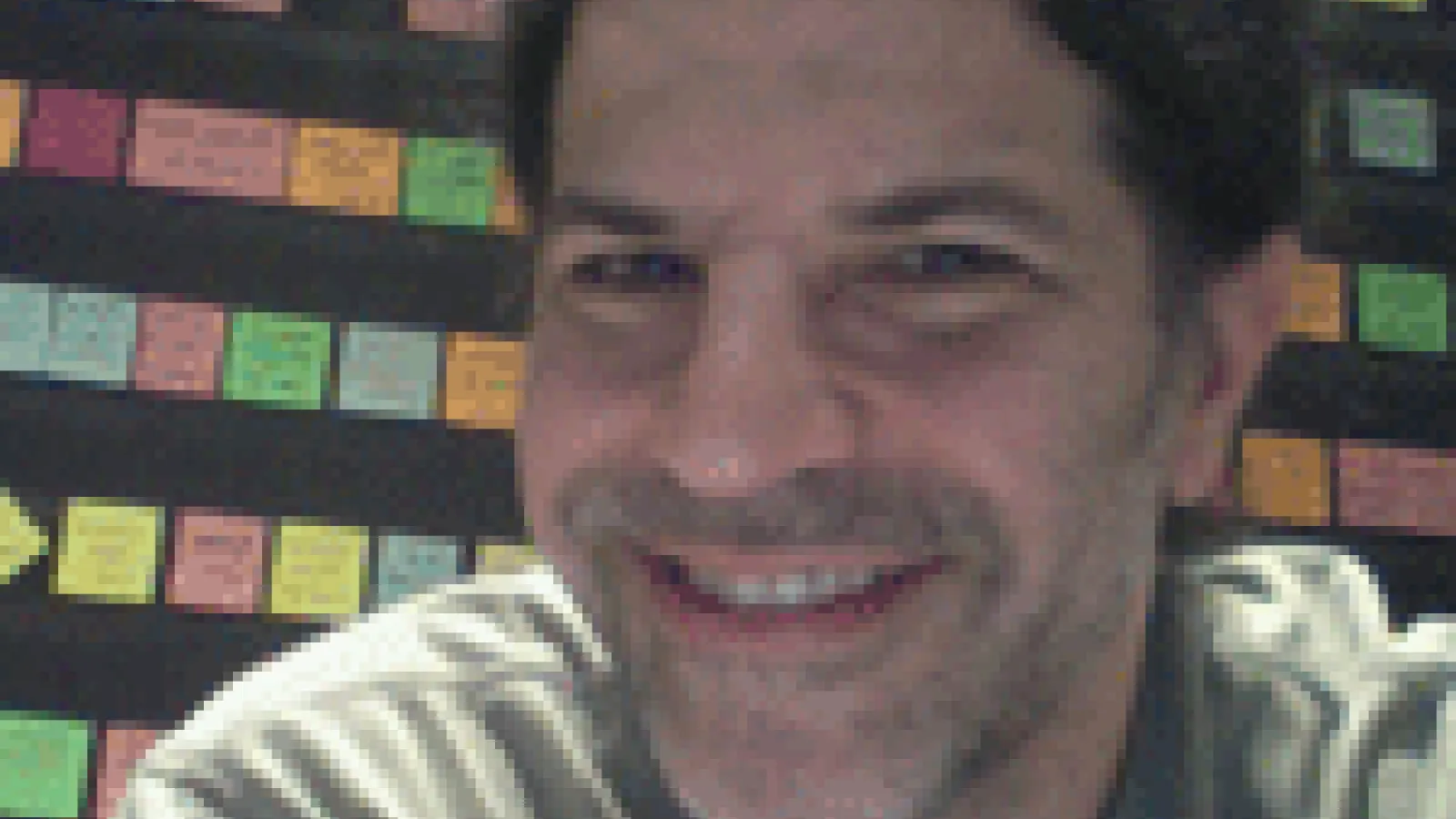 David Kaplan smiling with rows of sticky notes on wall behind him