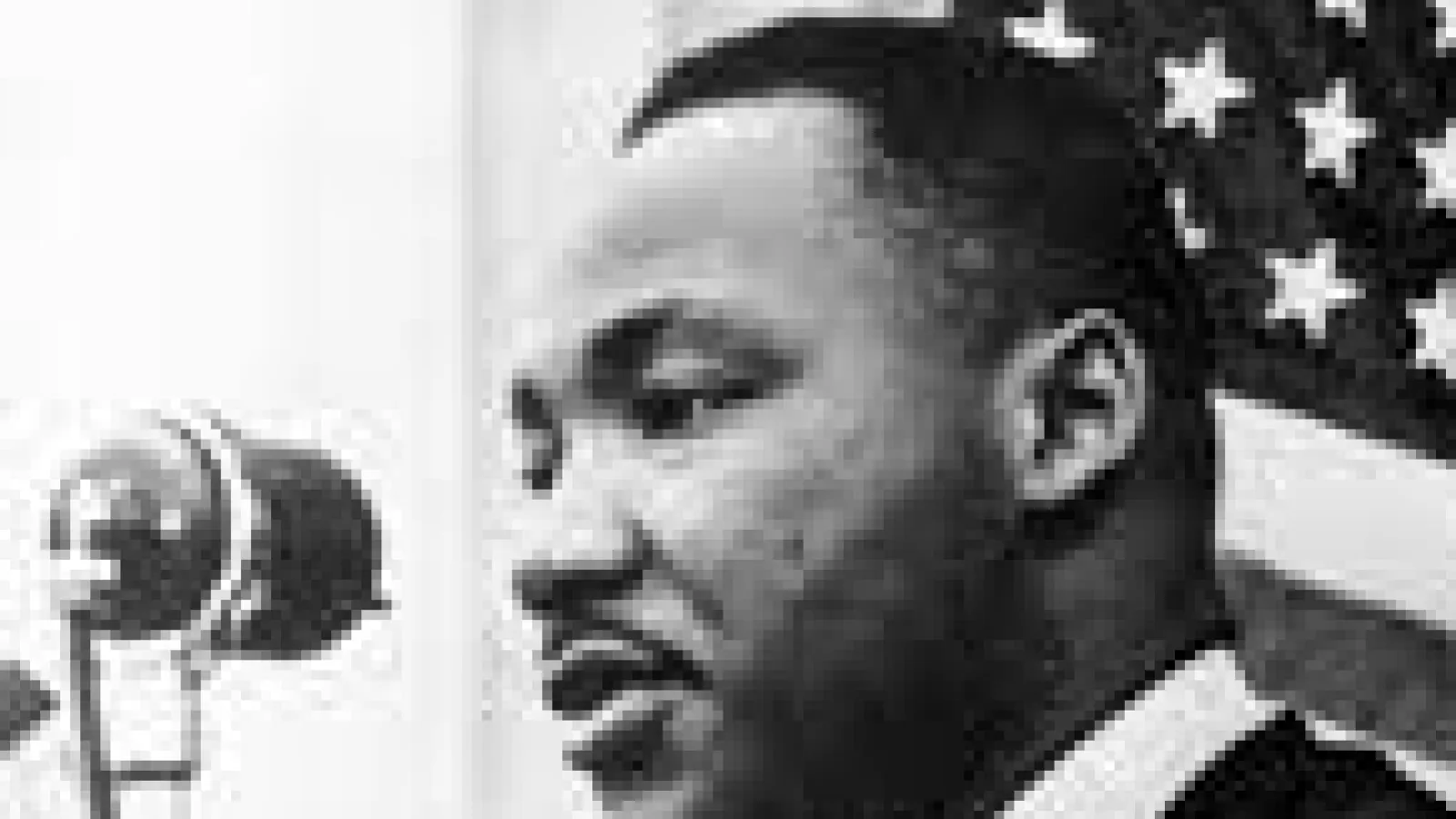 Black and white photo of Martin Luther King Jr Speaking into microphone with American flag in the background