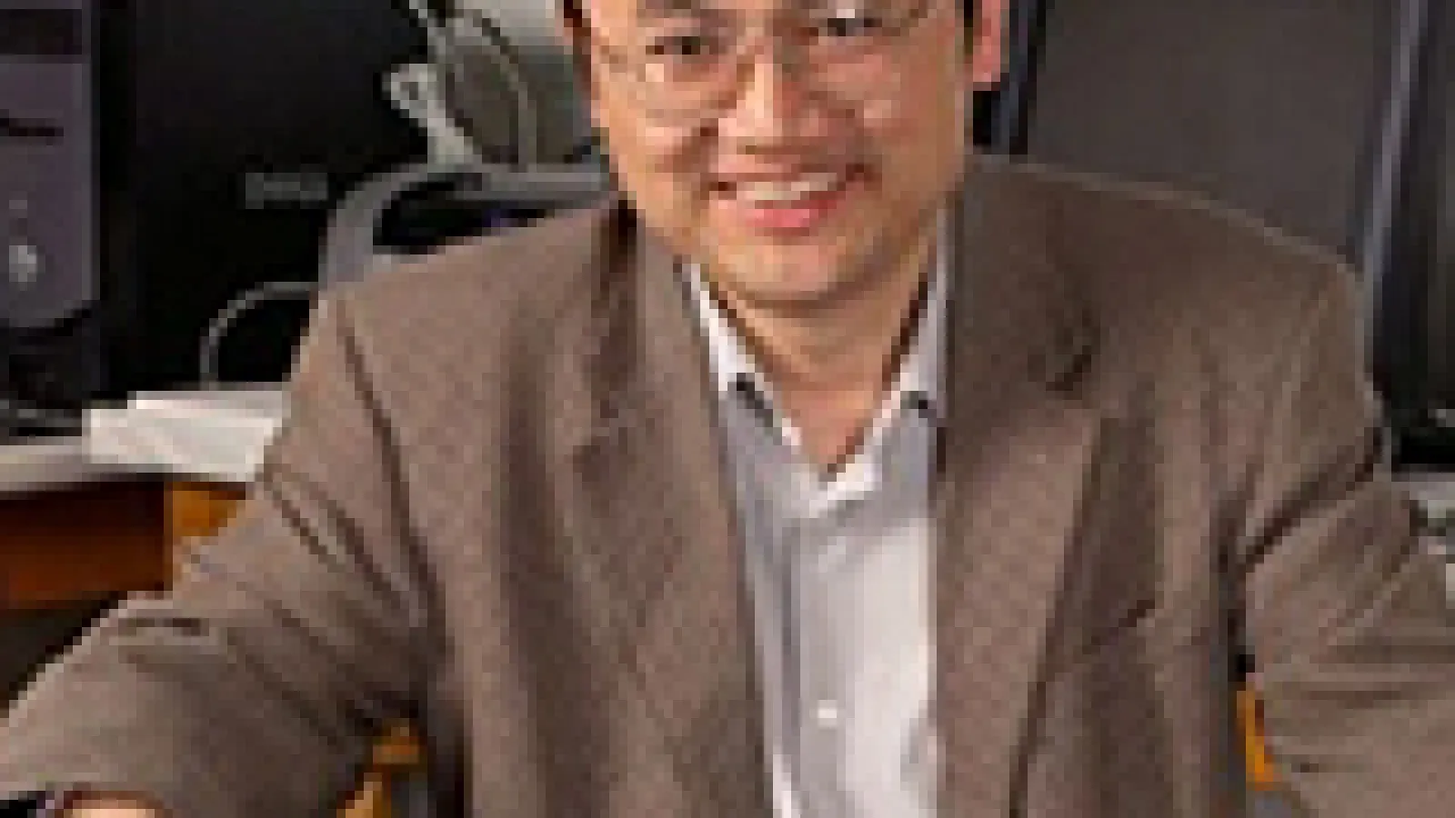 Dongping sitting on chair and smiling with computers in the background