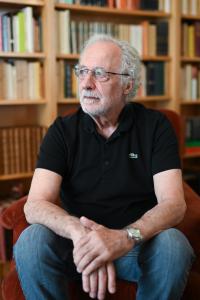 Pierre Agostini seated with blurred bookshelf behind him