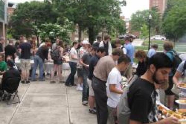 A picture from the physics picnic with students gathered around tables with food in a buffet style setting. 