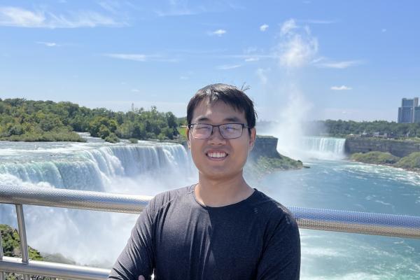 Photo of Dr. Penghao Zhu smiling in front of a large waterfall