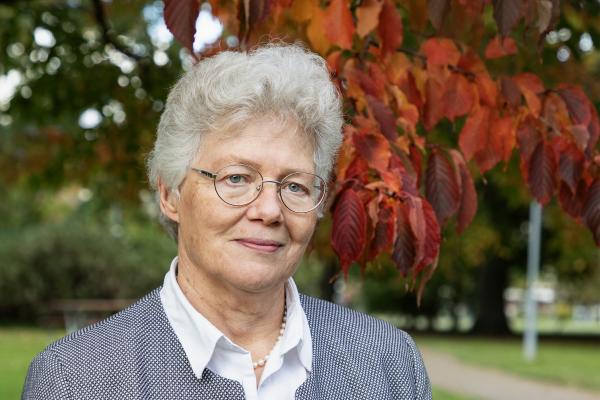 Photo of Anne L'Huiller with tree with bright orange leaves behind her.