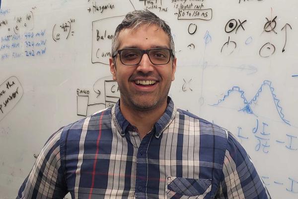 Professor Singh smiling with hands on hips in front of a whiteboard