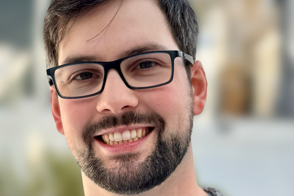 Alexander smiling in front of a blurred campus background