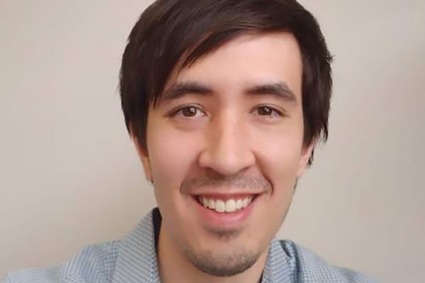 Matthew Low smiling in front of a plain beige wall
