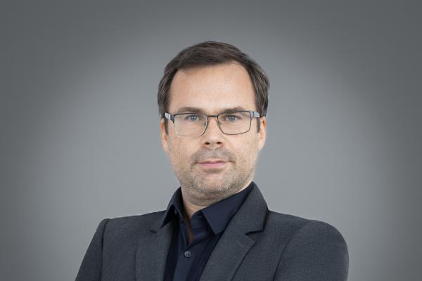 Nicolas standing with arms folded in front of a grey background
