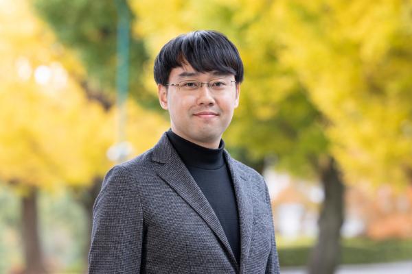 Yuki Fujimoto smiling and standing in front of a row of bright yellow trees