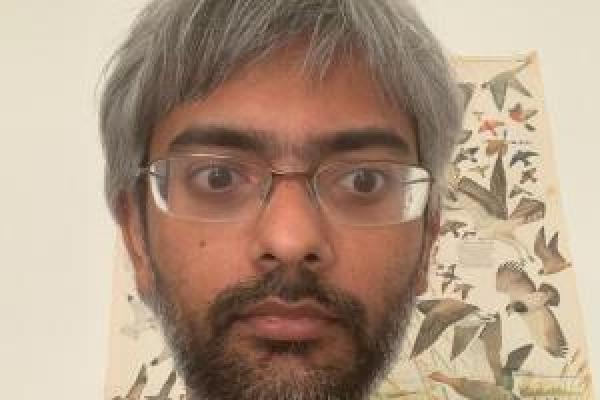 Sarang Gopalakrishnan in front of a beige wall and bird poster