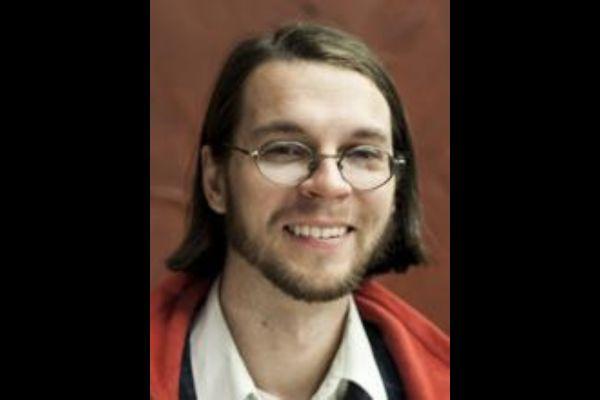 Chris Orban smiling with brown background and black frame border