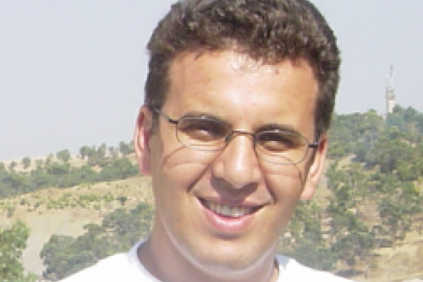 A close-up of Dr. Kramer Akli. The background contains trees and green hills.