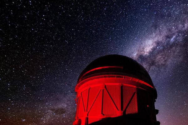 Large telescope lit up with red light and starry sky behind it