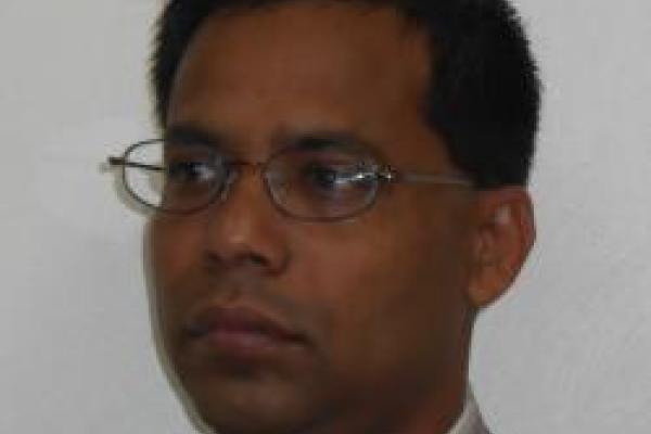 Theja De Silva in front of white background looking off to the side