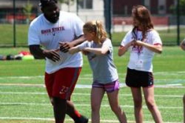 Two students on field with OSU football player