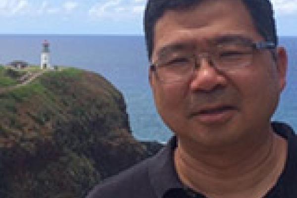 Roland Kawakami with lighthouse on a cliff far behind him