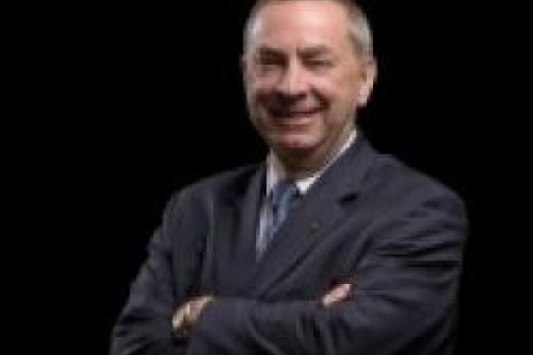 Nigel Lockyer smiling with arms crossed over chest, on black background
